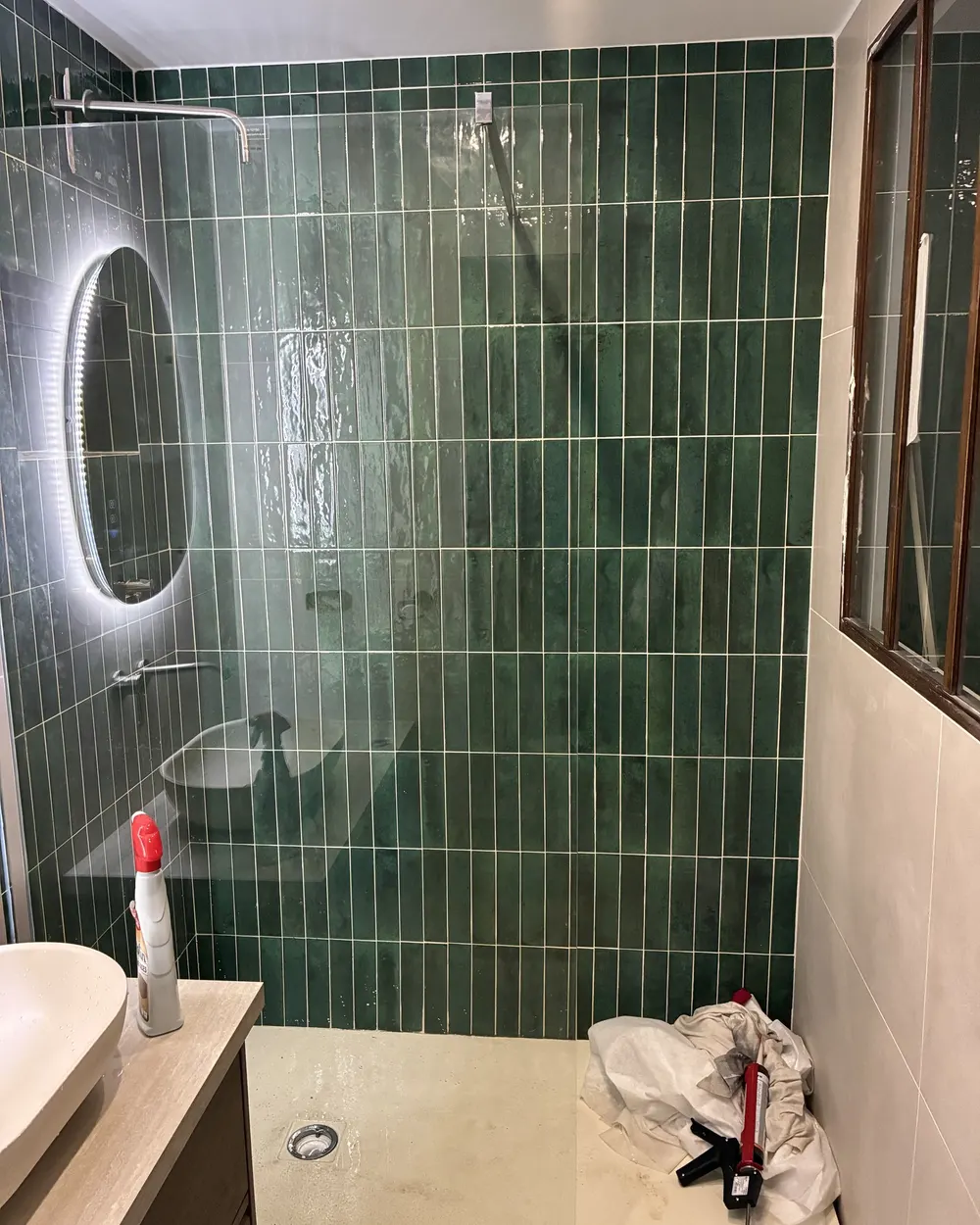 Salle de bain après rénovation : carrelage vert, vasque et miroir lumineux