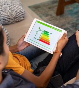 Rear view of indian couple checking on digital tablet housing energy efficiency rate. Young couple searching new green house on digital tablet. Husband embracing wife while checking the energy efficiency status of their home.